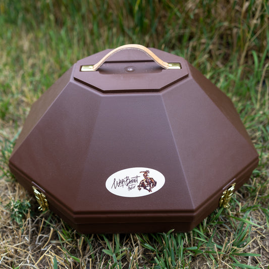 A brown octagonal hat can with a top handle, resting on grass. It features a white oval sticker on the front with a logo and the text 'Warbonnet Hats'.
Large enough to fit a 5 inch brim hat. 