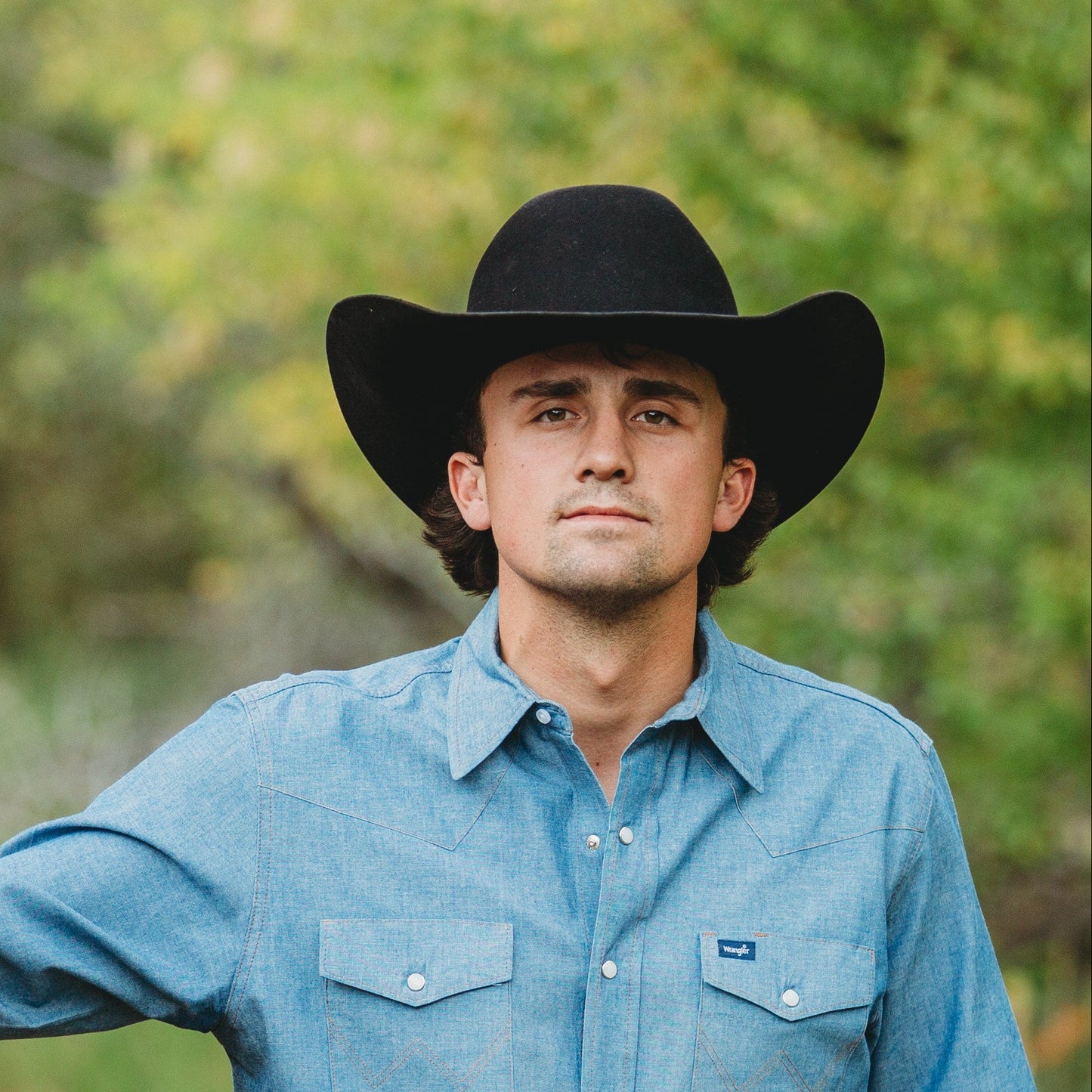 Man in a cowboy hat standing next to a horse on a trail