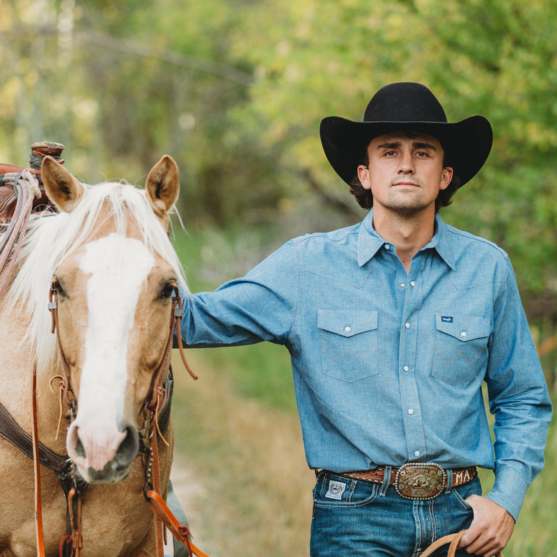 Man in a cowboy hat standing next to a horse on a trail